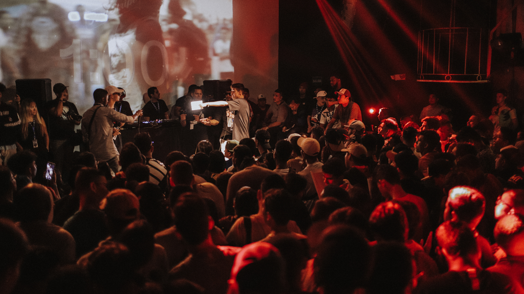 A lively hip-hop scene featuring a man on stage, surrounded by an enthusiastic crowd of people immersed in the performance.